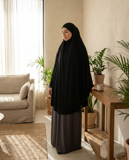Woman wearing flowing black Vaelora jersey khimar in warm interior