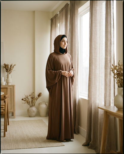 Woman wearing brown hooded abaya dress with hood up in a warm minimal interior