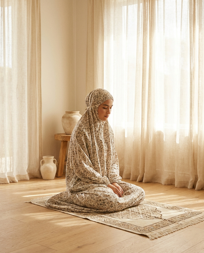 Woman wearing floral one-piece prayer dress sitting peacefully on a prayer mat